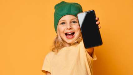 Ein Mädchen mit grüner Mütze lächelt mit einem Smartphone in der Hand.