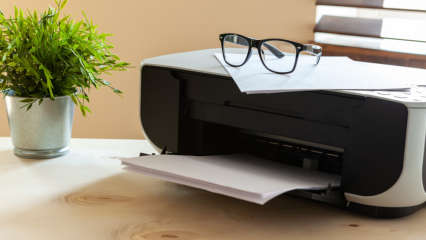 Auf einem Drucker liegen ein Stapel Papier und eine Brille.