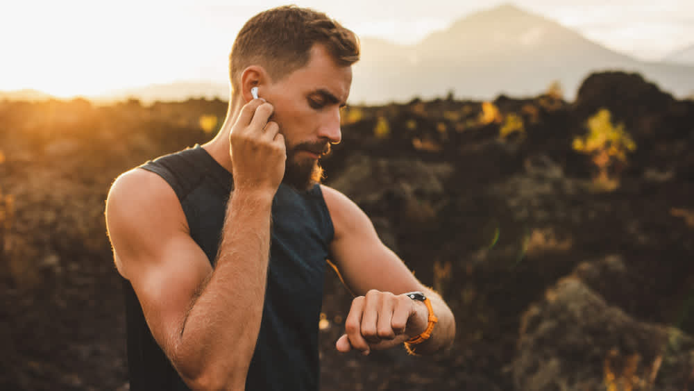 Ein Mann steckt sich einen Kopfhörer ins Ohr und schaut währenddessen auf seine Smartwatch.