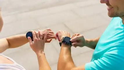 Zwei Personen stehen nebeneinander und tippen auf ihre Fitnessuhren.