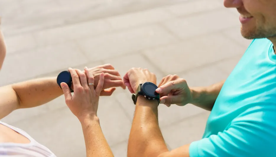 Zwei Personen stehen nebeneinander und tippen auf ihre Fitnessuhren.