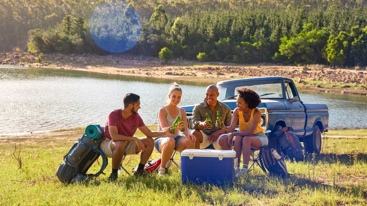 Vier Freunde sitzen mit einer Kühlbox am See.
