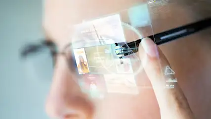 Nahaufnahme einer Person mit einer Datenbrille, die digitale Informationen auf dem Glas anzeigt. Ein Finger berührt die Fassung.