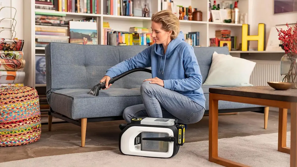 Eine Frau reinigt ein Sofa mit dem Kärcher SE 3-18 Compact.