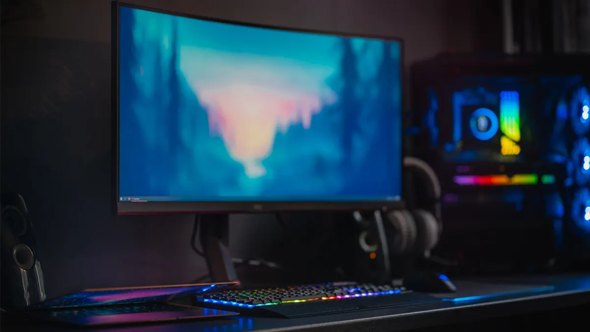 Ein Schreibtisch mit einem Monitor, einem PC-Turm mit violetten Lüftern, einer Tastatur, einer Maus und Kopfhörern.