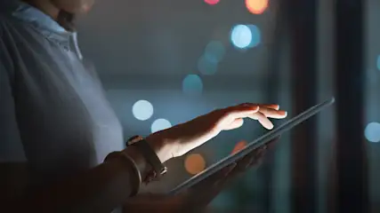 Eine Person im Hemd bedient ein Tablet; Uhren am Handgelenk. Bokeh-Lichter im Hintergrund.