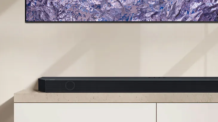 Auf einer hellen Kommode steht eine schwarze Soundbar. Über der Kommode hängt ein gerahmtes, abstraktes Bild in Lila- und Blautönen.