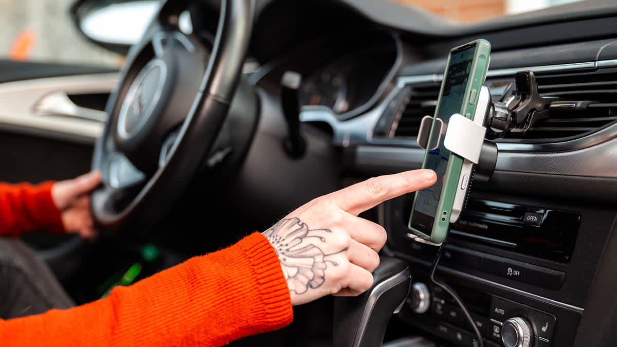 Eine Person bedient ein Smartphone im Auto in einer Halterung für die Lüftungsschlitze.