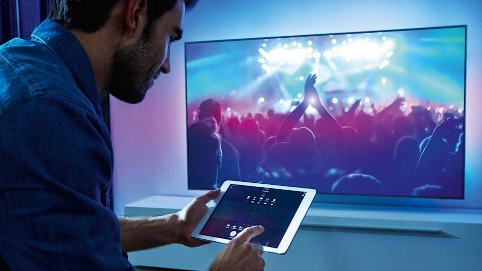 Mann benutzt ein iPad vor einem Philips-Fernseher.
