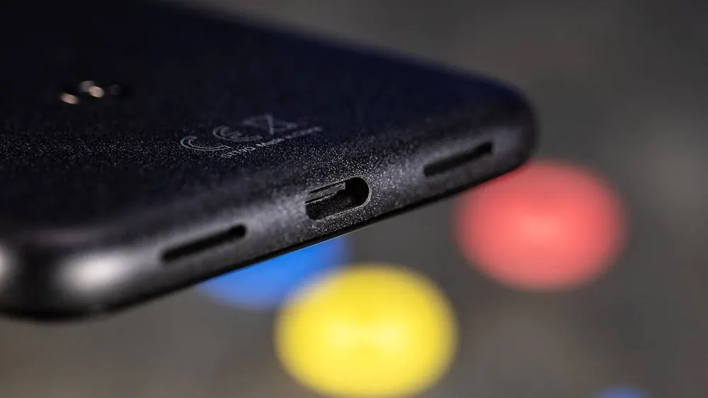Nahaufnahme eines schwarzen Smartphones mit USB-C-Anschluss und Lautsprecheröffnungen. Farbige Kreise im Hintergrund.