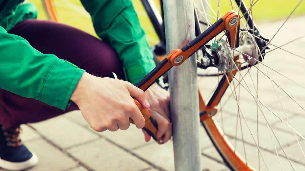 Eine Person schließt ein Fahrrad mit einem Faltschloss an einem Straßenschild an.