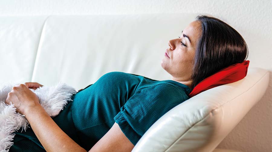 Eine Frau liegt auf einer weißen Couch mit einem roten Kissen unter dem Kopf und einer Decke.