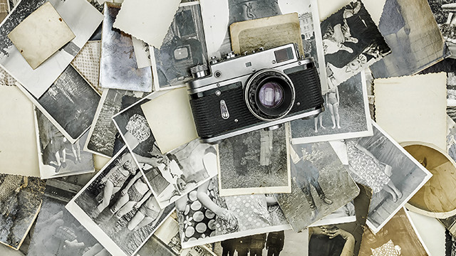Eine silberne und schwarze Kamera liegt auf einem Stapel alter Schwarz-Weiß-Fotografien und leerer Fotopapierstücke.