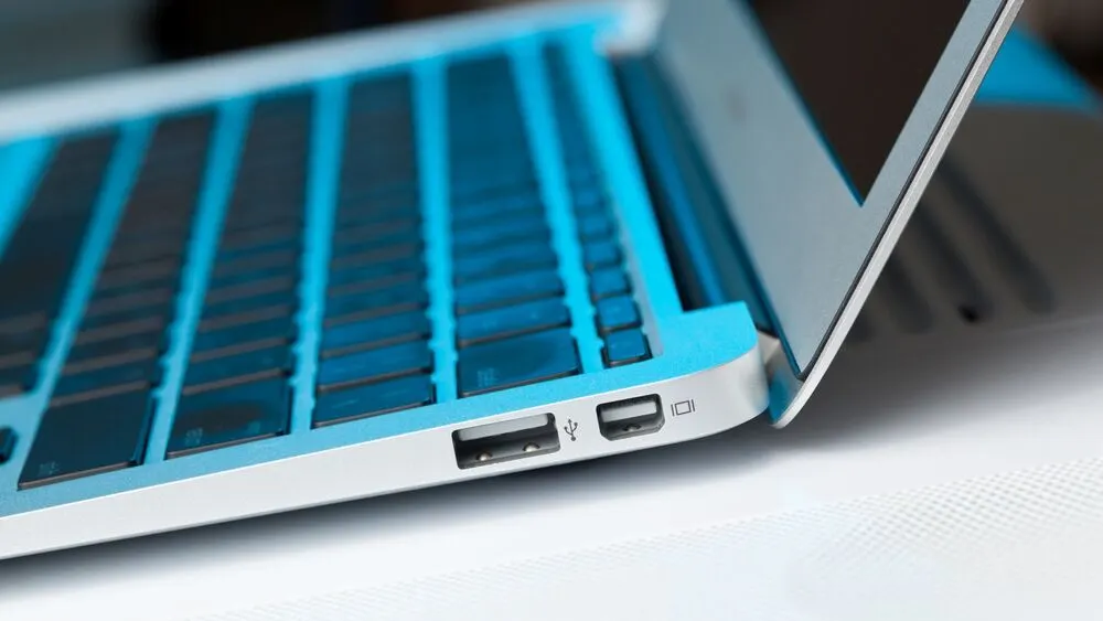 Nahaufnahme eines silbernen Laptops mit sichtbarer Tastatur und USB-Anschlüssen auf einem weißen Untergrund.