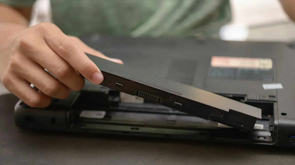 Eine Person baut den Akku aus einem Laptop aus.