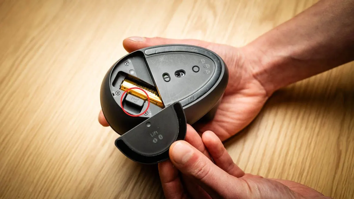 Alex öffnet die Unterseite der Logitech Lift: Im Batteriefach sitzt der USB-Dongle, er ist mit einem roten Kreis markiert.