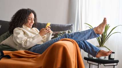 Eine junge Frau liegt auf dem Sofa mit einem gelben Handy in de Hand.