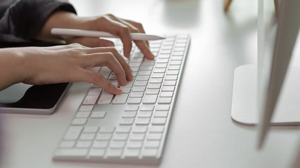Eine Person mit einem Apple Pencil in der Hand tippt auf einem Apple Magic Keyboard.