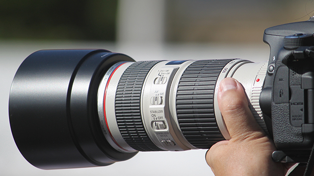 Nahaufnahme einer schwarzen Kamera mit einem grossen, mehrfarbigen Objektiv, das von einer Hand gehalten wird.