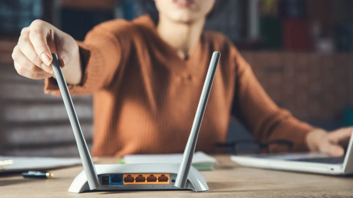 Eine Frau sitzt vor einem Laptop und berührt die Antenne eines Internetrouters.