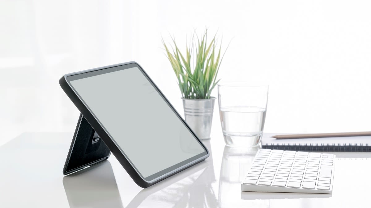 Ein Tablet mit Ständer steht auf einem Schreibtisch mit einer weißen Tastatur.