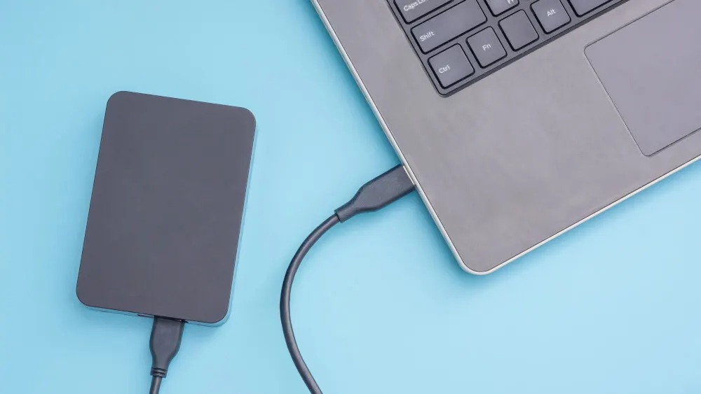 Ein graues Notebook ist mit einem USB-Kabel mit einer externen Festplatte auf blauem Hintergrund verbunden.