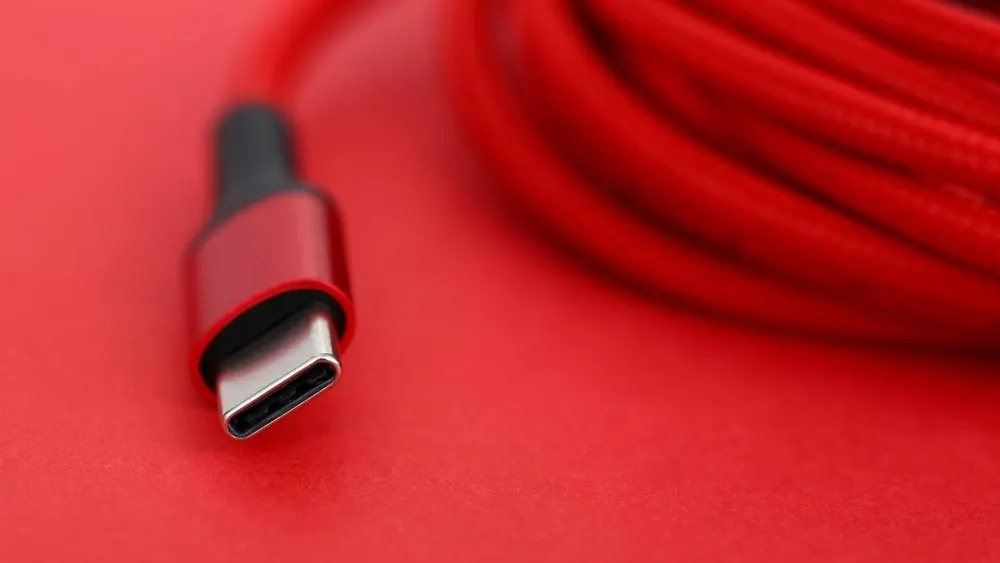 Rotes USB-C-Kabel mit grauem Stecker auf rotem Hintergrund. Das Kabel ist aufgerollt und liegt auf einer roten Oberfläche.