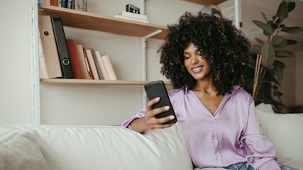 Junge Frau hält ihr Smartphone in der Hand und lächelt.