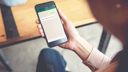 Eine Person hält ein Smartphone in der Hand auf dessen Bildschirm ein Chat-Messenger zu sehen ist