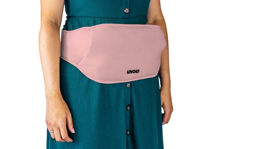 Eine Person trägt ein grünes Kleid mit Knöpfen und einen rosafarbenen Bauchgurt der Marke "Unold" um die Taille.