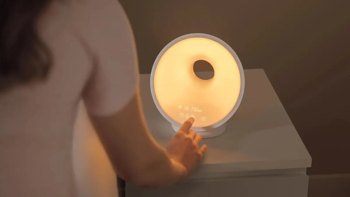 Eine Frau berührt die Touchanzeige des Lichtweckers Philips HF3654/01.