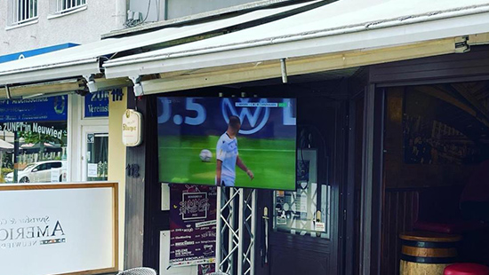 Auf Fernseher läuft ein Fußballspiel im Außenbereich vor der Sportsbar.