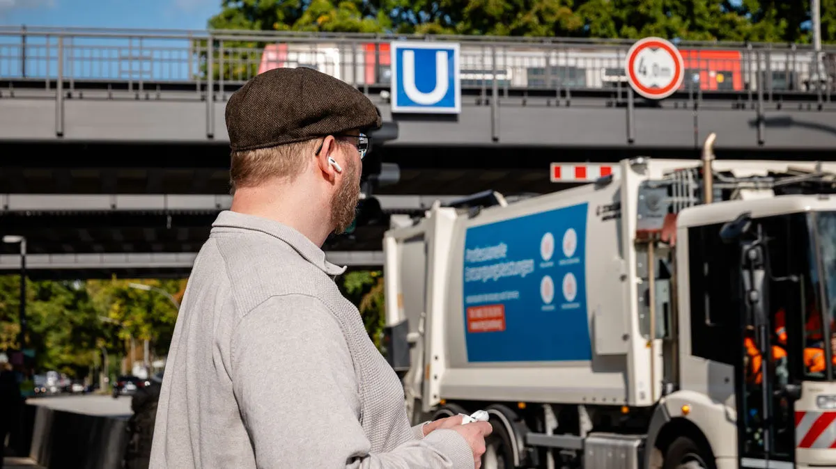 Andreas trägt die AirPods Pro 3 an einer befahrenen Straße und einer U-Bahn-Brücke.