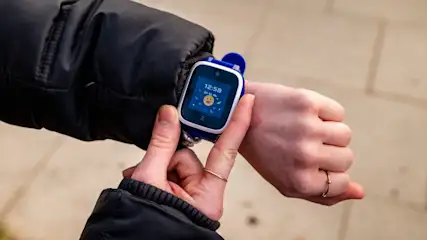 Eine Person trägt eine blaue Smartwatch am Handgelenk und berührt sie mit der anderen Hand.