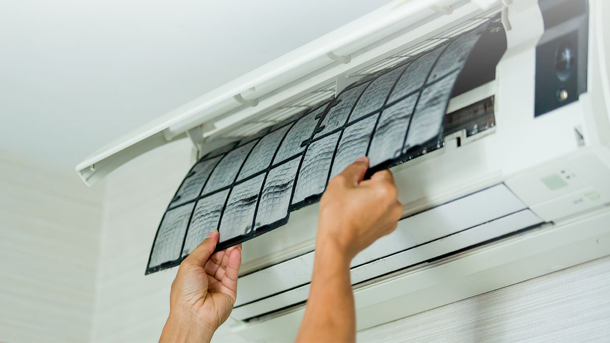 Zwei Hände entfernen die Filter einer geöffneten Klimaanlage an der Wand.