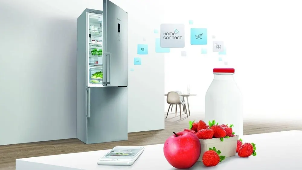 Ein Kühlschrank mit offener Tür, ein Smartphone und ein Tisch mit Erdbeeren, Apfel und einer Flasche.