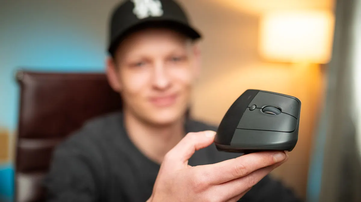 Alex zeigt die ergonomische Maus Logitech Lift mit der Schrägseite zur Kamera.