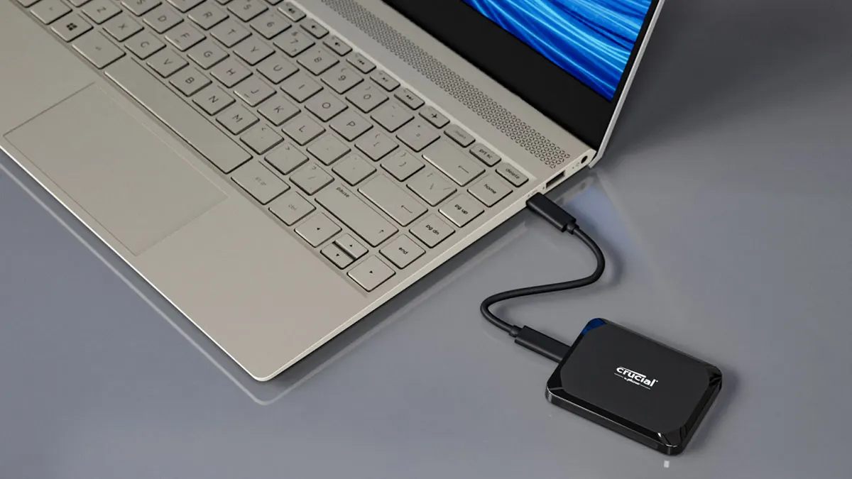 Ein Laptop mit Tastatur ist mit einer externen schwarzen Crucial-Festplatte über ein schwarzes Kabel verbunden.