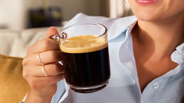 Eine Person hält eine Tasse Kaffee mit Schaum vor einem blauen Hintergrund.
