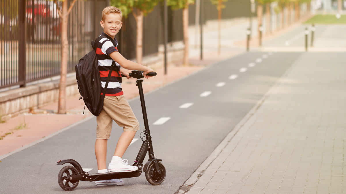 Ein Junge mit Rucksack posiert auf einem E-Scooter.