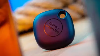 Ein dunkler Galaxy SmartTag mit Loch für den Schlüsselanhänger liegt auf einer hellen, leicht verschwommenen Oberfläche.