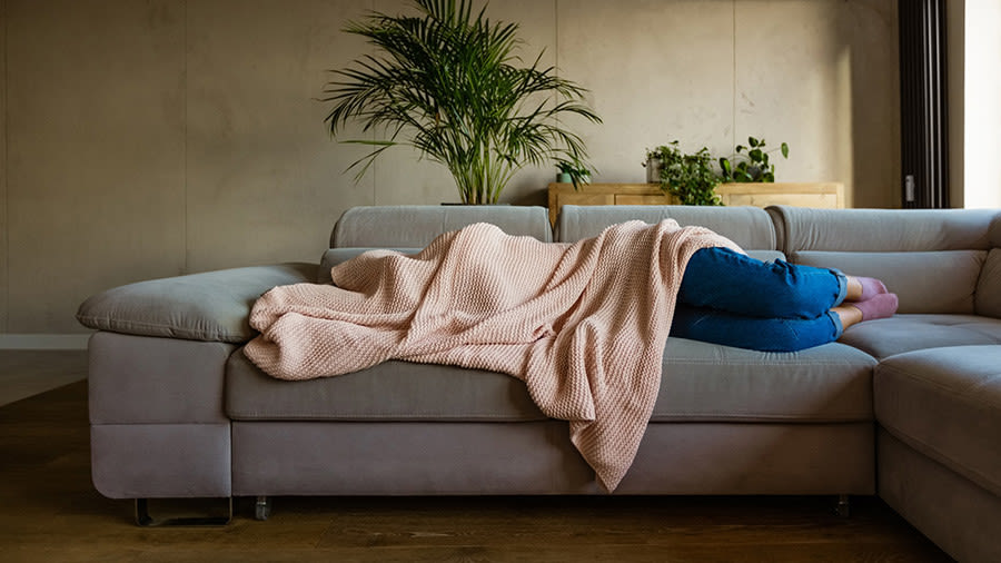 Frau liegt zugedeckt auf einer Couch mit Decke