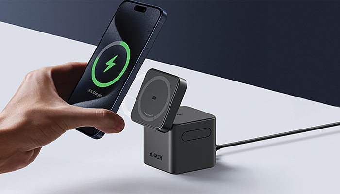 Hand hält Smartphone mit grünem Ladesymbol über schwarzer kabelloser Ladestation auf weißem Schreibtisch.