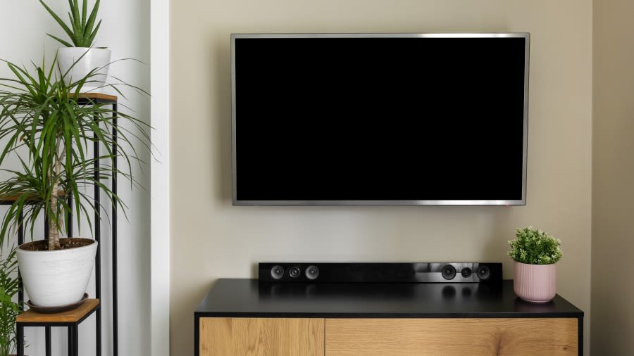 Ein TV hängt an der Wand. Auf der Kommode darunter steht eine Soundbar. 