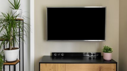 Ein TV hängt an der Wand und darunter steht auf einer Kommode eine Soundbar.