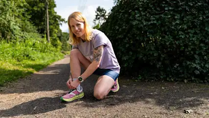 Franzi trägt die Samsung Galaxy Watch8 am Handgelenk und schnürt ihre Laufschuhe auf einem Weg im Park.