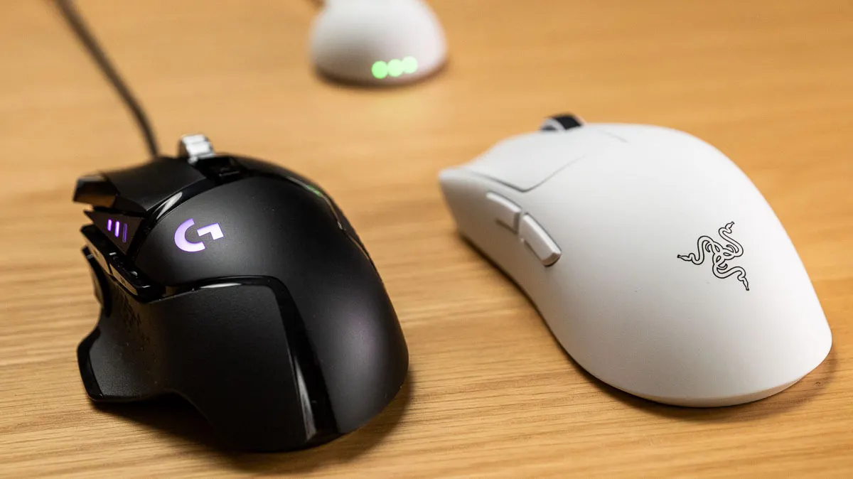 Die Logitech G502 Hero (links) und die Razer Viper V4 Pro liegen auf einem Holztisch.