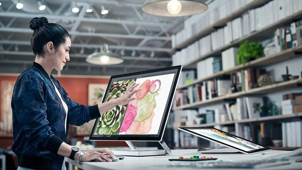 Eine Frau mit Jacke bedient einen Computer mit Grafikdisplay. Bücherregale stehen im Hintergrund.