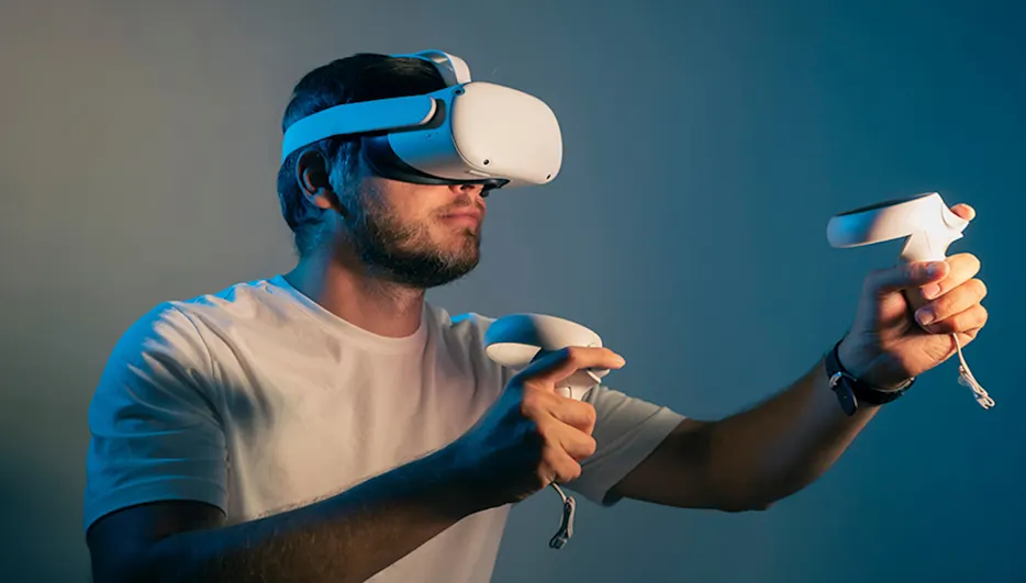Ein Mann mit weißem T-Shirt trägt ein VR-Headset und hält zwei weiße Controller vor einem blauen Hintergrund.