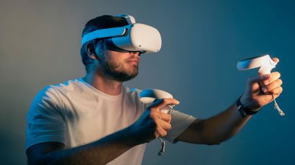 Ein junger Mann trägt eine Meta Quest 2 VR-Brille und bewegt sich mit den Controllern in den Händen.